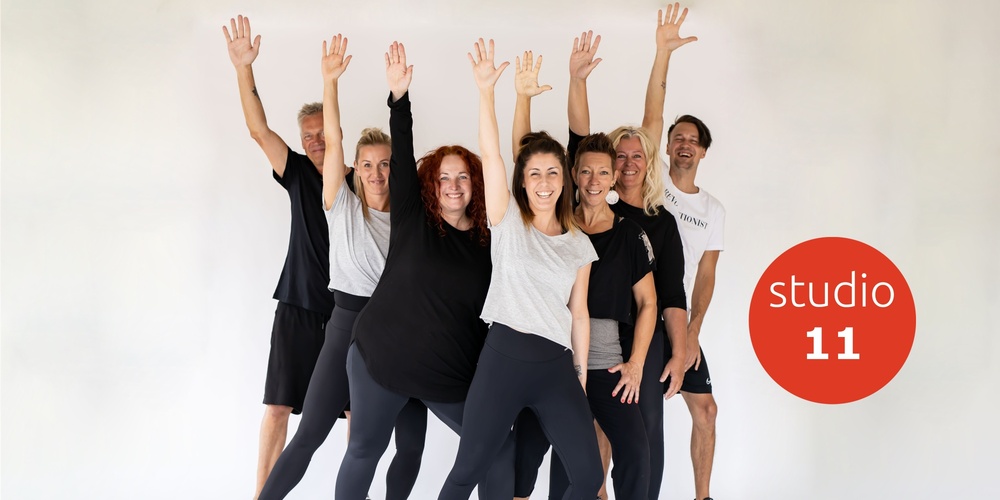 En grupp glada vuxna i träningskläder poserar med armarna uppsträckta framför en vit bakgrund.