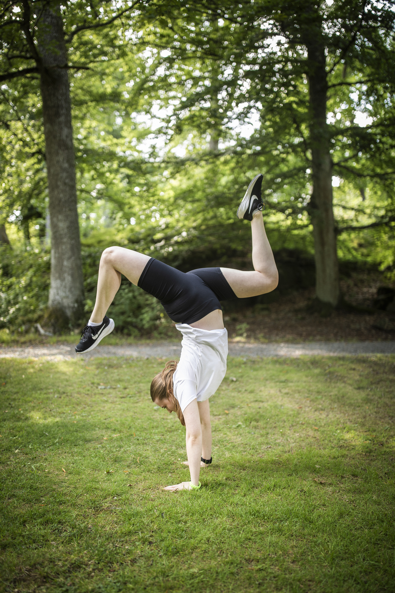 En person gör en handvolt på gräset i en grönskande park.