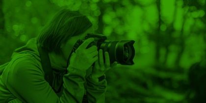 Person fotograferar i skogen med en kamera, bilden har ett grönt filter.