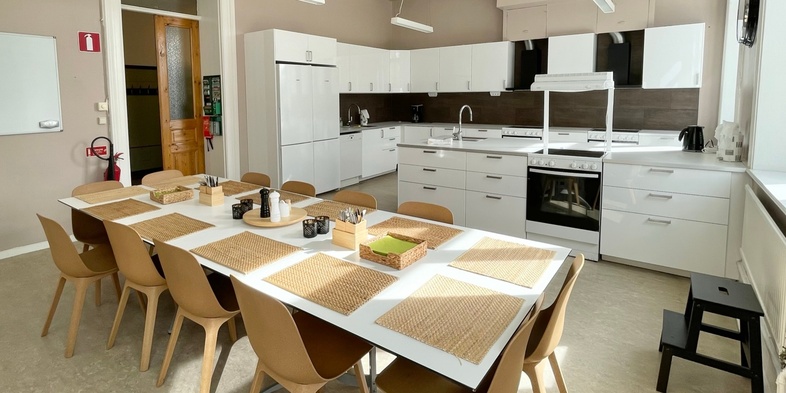 Ljust och modernt kök med lång matplats, vita skåp och trästolar, inga människor syns.