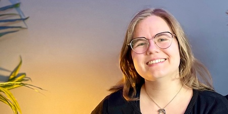 Två leende personer sitter tillsammans i en blå soffa i ett rum med blå vägg och grön växt.