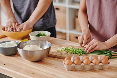 Två personer förbereder mat, en hackar grönsaker och en blandar ingredienser i en skål.