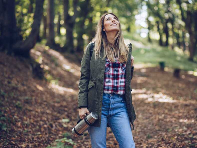 En person står i en grön skog med en termos i handen.