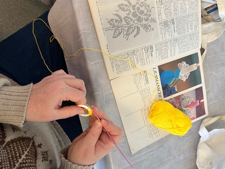 Person virkar med gult garn och virknål, bredvid ett mönster i en handarbetstidning.