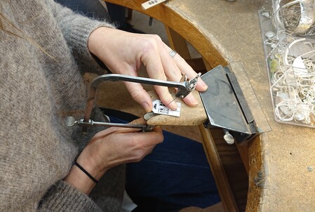 En person använder en juvelersåg för att arbeta med metall vid ett arbetsbord.