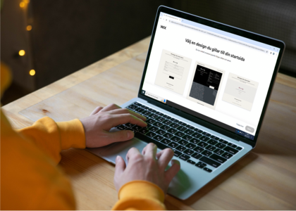 Person i gul tröja använder en bärbar dator på ett träbord, skärmen visar en webbsida om designval.