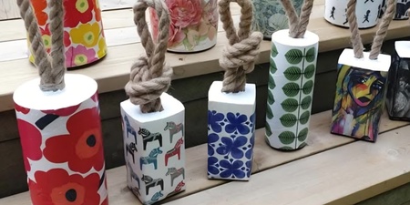 Färgglada dörrstopp i betong med rep och olika mönster står uppradade på en trätrappa utomhus.