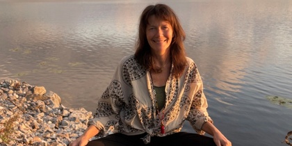 Kvinna sitter i meditationsställning på en brygga vid en sjö i solnedgången.