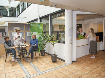 Väntrum på vårdcentral med sittande och stående personer samt reception.