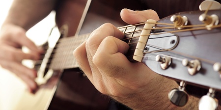Närbild av en person som spelar akustisk gitarr, fokus på vänster hand på gitarrens greppbräda.