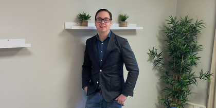 En person står vid väggen i ett mötesrum med bord, stolar, växter och hyllor med krukväxter.