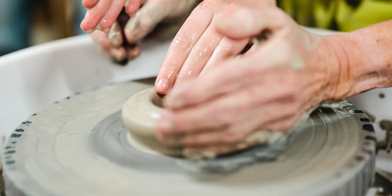 Två personer formar lera på en drejskiva med sina händer under en keramikkurs.