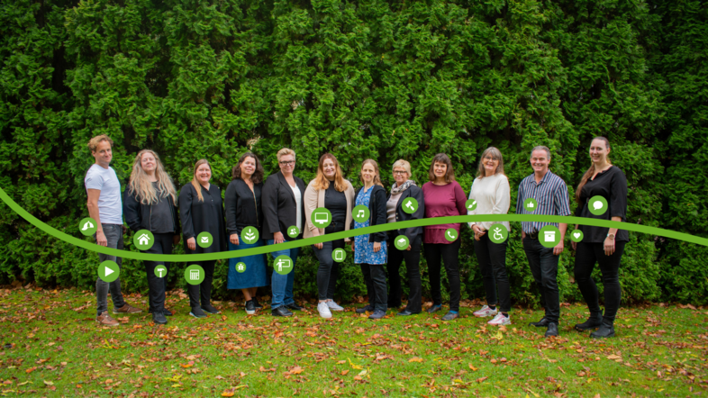 En grupp människor står på gräsmatta framför en grön häck, med gröna ikoner framför sig.