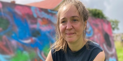 En kvinna sitter på huk på gräs framför en färgglad graffitivägg utomhus.