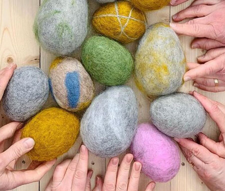 Flera händer håller i färgglada tovade ullstenar på ett ljust träbord.