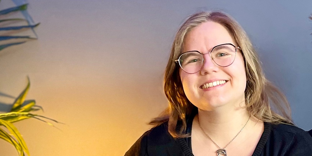 Två leende personer sitter tillsammans i en blå soffa i ett rum med blå vägg och grön växt.