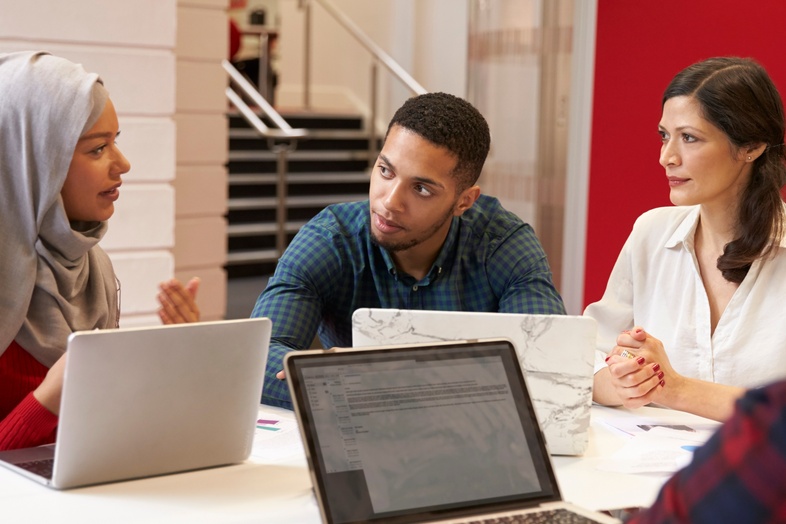 Fyra personer sitter runt ett bord med bärbara datorer och diskuterar i en modern kontorsmiljö.