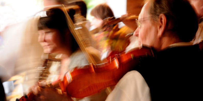 Suddig bild av personer som spelar fiol i en livlig miljö, rörelseoskärpa dominerar.