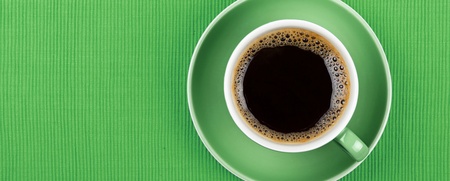 En kopp svart kaffe i en grön kopp och fat, sedd uppifrån på en grön bakgrund.