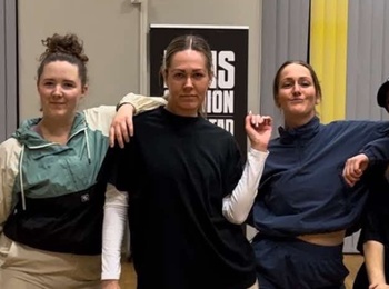 Fyra personer poserar tillsammans i en dansstudio med trägolv och gråa gardiner.