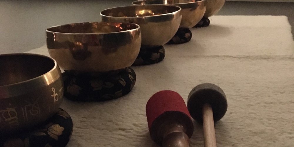 Fem tibetanska klangskålar står på rad på en matta med två klubbor framför dem i ett dämpat rum.