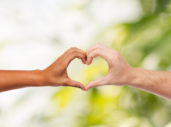 Två händer i olika hudtoner formar ett hjärta mot en suddig grön bakgrund.