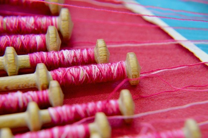 Närbild av flera trådrullar med rosa tråd på ett rött tygstycke.