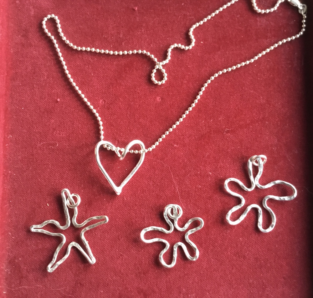 Smycken av silvertråd på röd sammet, inklusive ett hjärthalsband och tre stjärn- och blomformade hängen.