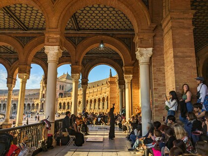 En flamencodansare uppträder inför en publik under valv på Plaza de España i Sevilla, med soligt väder utomhus.