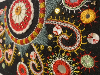Närbild av färgglad broderad textil med speglar, pärlor och snirkliga mönster på svart tyg.