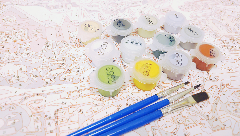 Färglådor och penslar ligger på en målarbok med numrerade fält för paint by numbers.