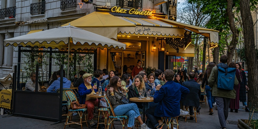 Uteservering på ett franskt café med människor som samtalar och äter under en gul markis.