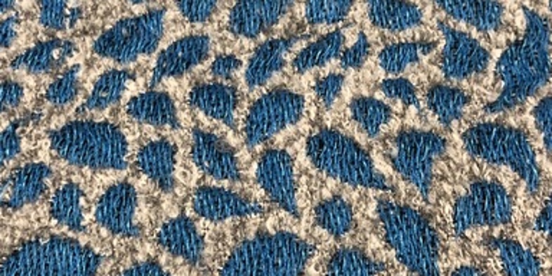 Närbild av ett tyg med blå och beige mönster som liknar djurfläckar eller blad.