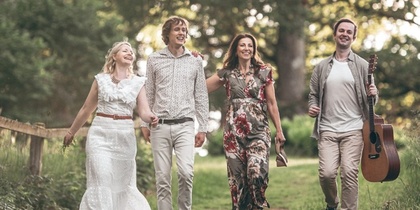 Fyra personer går tillsammans på en grön stig i naturen, en bär en gitarr.