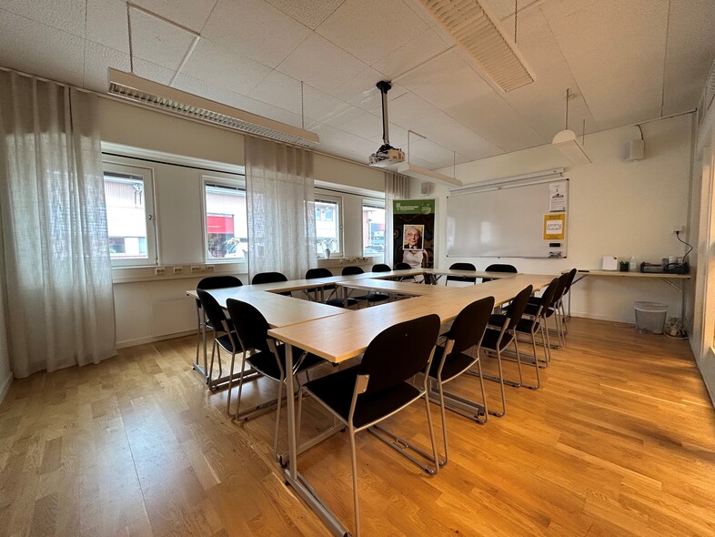 Ett ljust konferensrum med rektangulärt bord, svarta stolar, whiteboard och stora fönster.