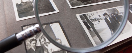 Ett fotoalbum med svartvita fotografier granskas med ett förstoringsglas.