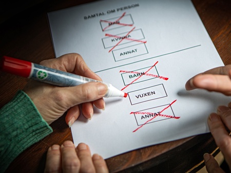 Två händer markerar och kryssar i rutor på ett formulär med en röd penna.