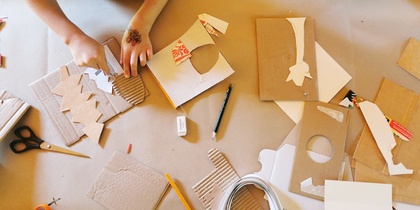 Två barn pysslar med kartong, saxar och pennor på ett bord.