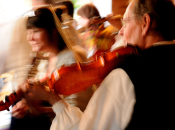 Suddig bild av personer som spelar fiol i en livlig miljö, rörelseoskärpa dominerar.