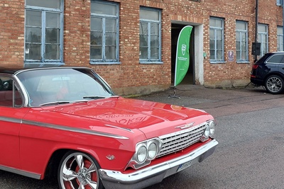 En röd klassisk bil står parkerad framför en tegelbyggnad med blå fönster.