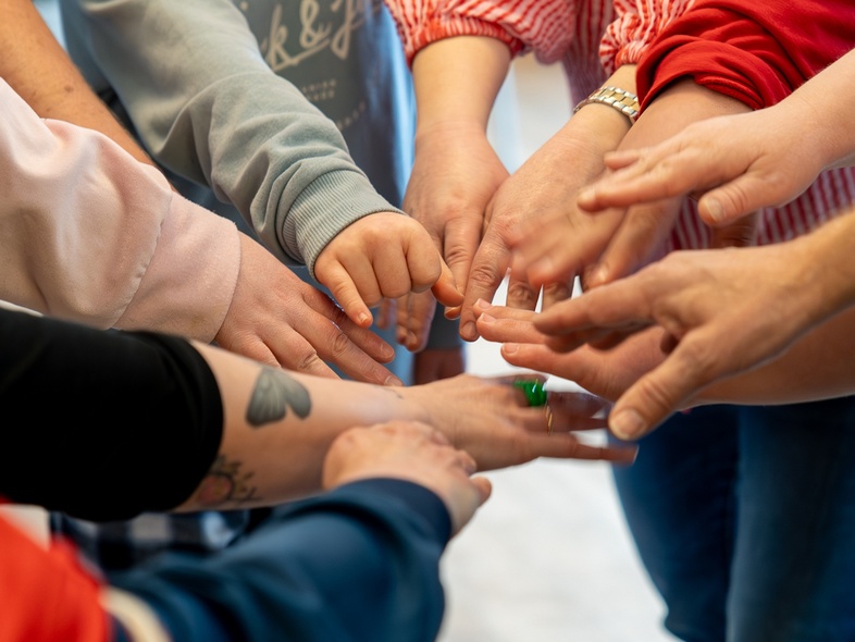 Flera personer sträcker in sina händer mot mitten i en gemensam cirkel, fokus på händerna.