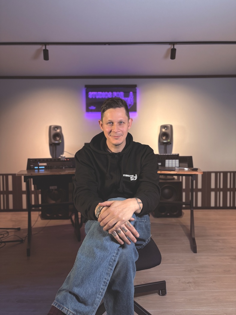 Man sitter på en stol i en modern musikstudio med ljudutrustning och högtalare bakom sig.