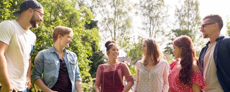 Sex unga vuxna står utomhus i en park och pratar med varandra en solig dag.