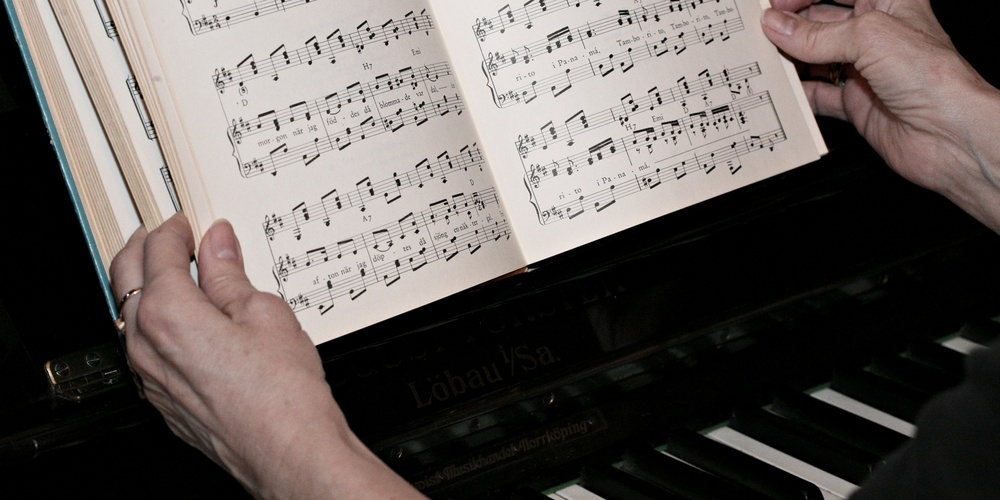 En person håller ett nothäfte ovanför ett piano, redo att spela efter noterna.