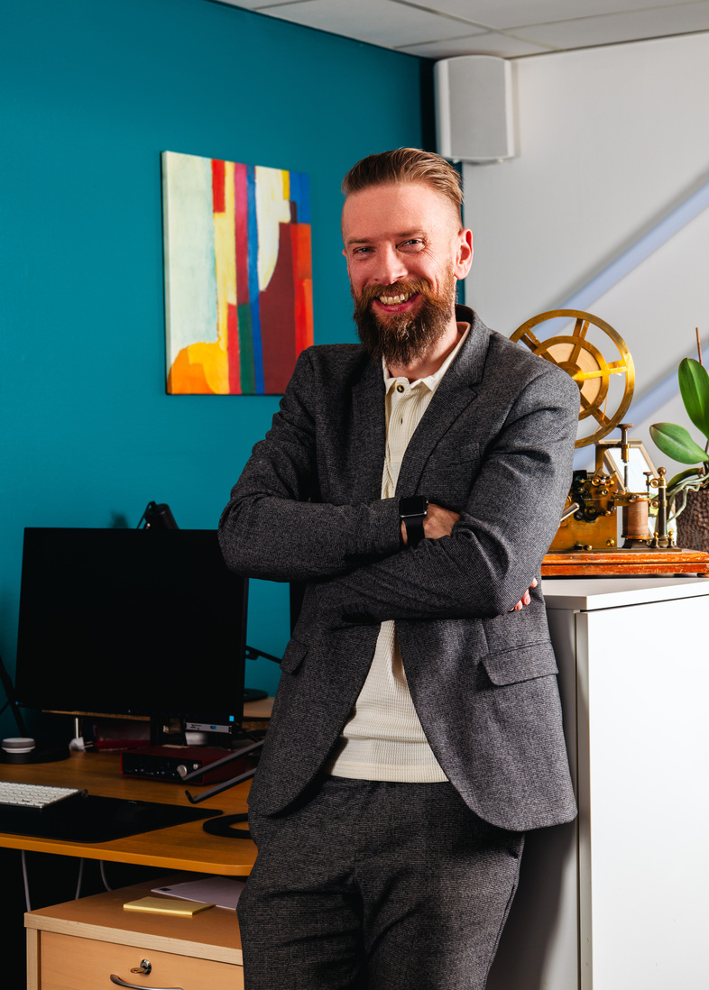 Per Pettersson står leende med armarna i kors i ett modernt kontor med färgglad tavla på väggen.