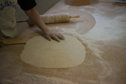 En person kavlar ut en stor, tunn deg på ett mjölat bord med en kruskavel.