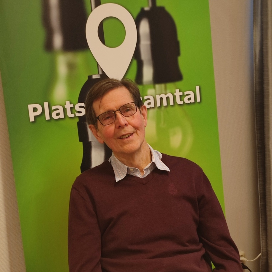 Man med glasögon sitter vid ett bord framför en grön skylt med texten 'Plats för samtal'.