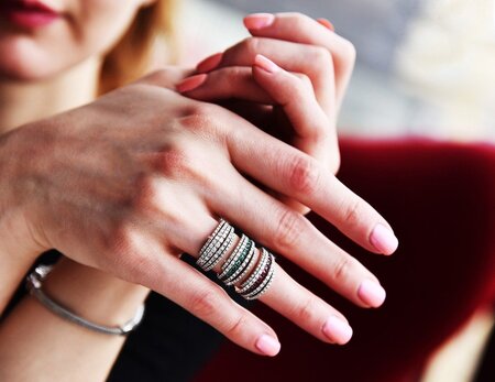 Närbild på händer med flera glittrande ringar och ljusrosa nagellack.