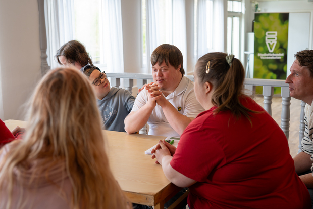 En grupp personer sitter runt ett bord och samtalar i ett ljust rum.