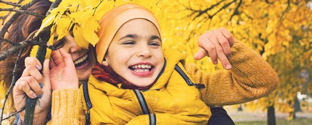 Ett barn och en vuxen skrattar tillsammans bland gula höstlöv utomhus.